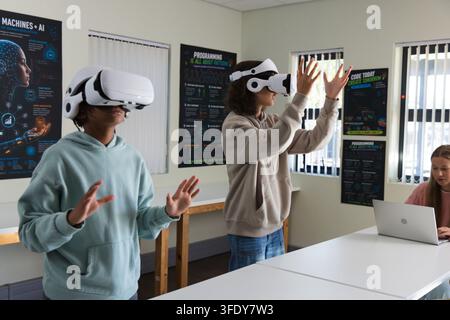 Diverse teens wearing white VR headsets interacting with VR in lab with silver laptop, AI posters Stock Photo
