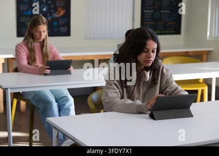 Diverse female students sitting in classroom at white tables, front-right student using tablet Stock Photo