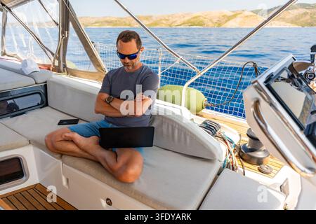 Thoughtful man sitting with laptop on a sailing yacht during a work break. Business planning and location independent lifestyle concept. Stock Photo