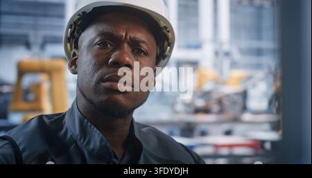 Close Up of African American Male Operator at High Tech Modern Control Desk, Supervises Automated Robotic Welding Via Computer Interface. Concept of AI Manufacturing, Industry 4.0 and Robotization. Stock Photo