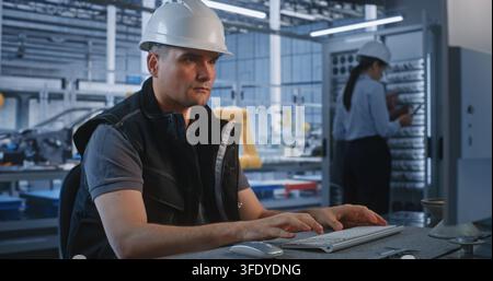 Inside Smart Factory Control Room, Engineer Operates PC while Colleagues Maintain Server Cabinet in Background. Industrial Automation and Server Infrastructure Optimize Manufacturing. Teamwork. Stock Photo