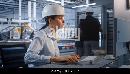 In Smart Factory, Female Engineer Uses Vernier Caliper to Inspect Metal Part at Desk. Male Colleagues Work at Large Server Cabinet Nearby to Ensure Smooth Automated Workflows. Concept of Industry 4.0. Stock Photo