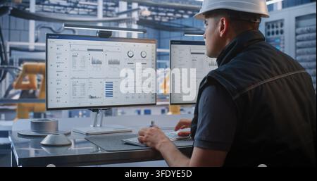 Technician Controls Robotic Arm Factory Operations Using CAD Software and Analytics on Monitor. Industry 4.0 Technology Drives Efficiency in Modern Automated Vehicle Assembly. AI Manufacturing. Stock Photo