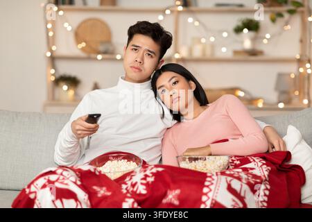 Bored Asian Couple Watching TV Celebrating Christmas At Home Stock Photo