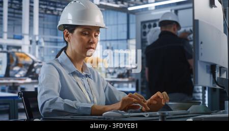 Professional Female Engineer Inspects Assembly of Automotive Frames at Workstation at High Tech Facility. Smart Industrial Automation and Server Maintenance Enhance Modern Automotive Manufacturing. Stock Photo