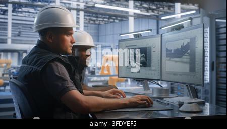 Caucasian Engineer and African American Colleague Discuss 3D Car Chassis Model on Dual Monitors in Smart Plant. Diverse Collaboration Accelerates Industry 4.0 Production. Concept of Professional Team. Stock Photo