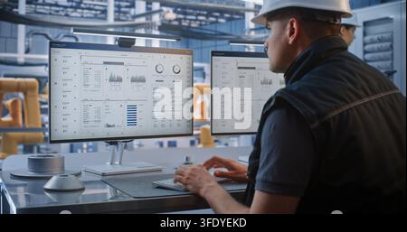 Young Engineer Analyzes Telemetry Data, Robotic Car Production Feeds on Monitor At High Tech Workstation. Modern Industrial Automation Enhances Precision in Smart Factory Manufacturing. Industry 4.0. Stock Photo