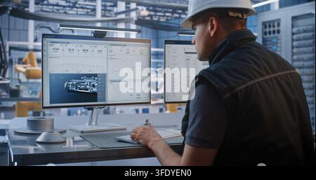 Young Engineer Analyzes Telemetry Data, Robotic Car Production Feeds on Monitor At High Tech Workstation. Modern Industrial Automation Enhances Precision in Smart Factory Manufacturing. Industry 4.0. Stock Photo