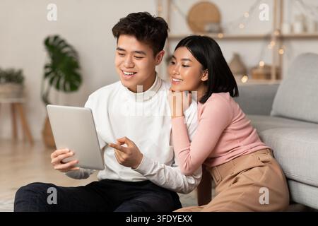 Young Asian Spouses Relaxing Using Digital Tablet Browsing Internet Indoors Stock Photo