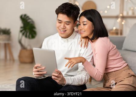 Japanese Millennial Couple Using Digital Tablet Sitting Together At Home Stock Photo
