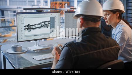 Female Engineer Points at 3D Car Chassis Screen while Discussing Component Design with Colleague Holding Prototype. Teamwork, CAD Software Drive Industry 4.0 Production Efficiency. Team Collaboration. Stock Photo