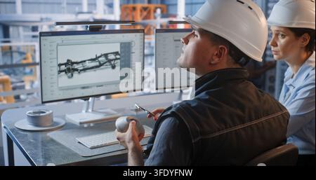 Female Specialist Points to CAD Graphics on Screen as Male Engineer Checks Machined Part with Caliper. Quality Assurance and Digital Twin Technology Optimize Smart Factory Automotive Workflows. Stock Photo