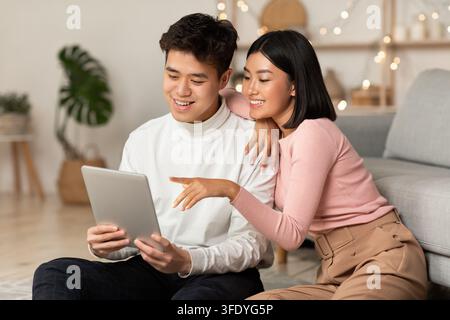 Japanese Boyfriend And Girlfriend Using Digital Tablet Sitting At Home Stock Photo
