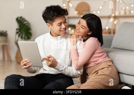 Asian Millennial Couple Using Digital Tablet Browsing Internet Indoors Stock Photo