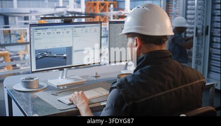 In Glass Control Room, Male Engineer Designs Car Chassis on PC as Robotic Arms Assemble Vehicles on Conveyor Line. Industry 4.0 Technology Drives Factory Efficiency. Concept of Robotization. Stock Photo