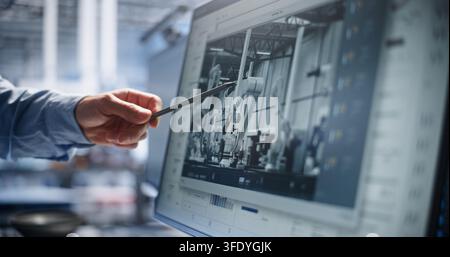 Engineer Points Pen at Computer Display to Analyze Robotic Assembly Workflows and System Diagnostics. Human Oversight Ensures Quality Control in Modern Smart Plants. Concept of Quality Inspection. Stock Photo