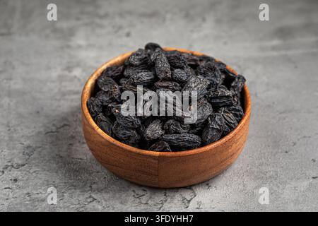 Black raisins in wooden bowl on stone background Stock Photo