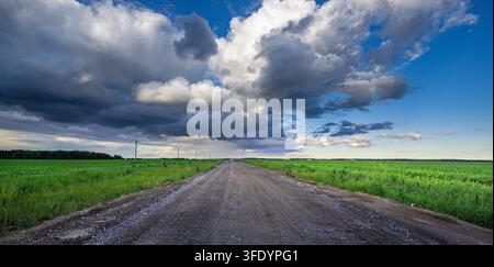Wide gravel path cuts through vibrant green fields. Sky swirls with dramatic, brooding clouds above Stock Photo