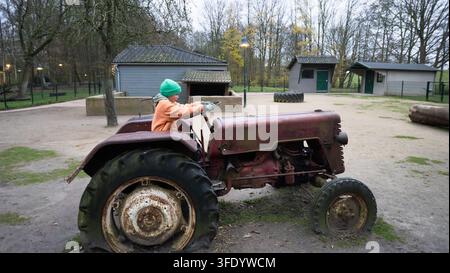 Boy in a green hat and orange shirt sitting on an old farm tractor in a park Stock Photo