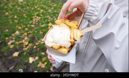 Hands holding crispy golden french fries with mayo in a paper cone outdoors Stock Photo