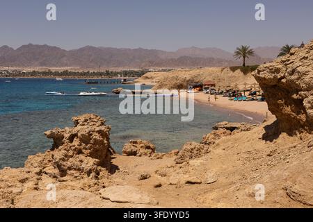 Clear turquoise water over a shallow coral reef near Movenpick Resort Sharm El Sheikh, Egypt, with the Red Sea coastline in the distance Stock Photo