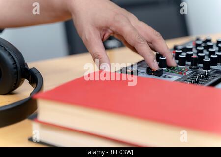 Close-up of a sound engineer's hand adjusting faders on a professional audio mixing console during a live broadcast session. Stock Photo