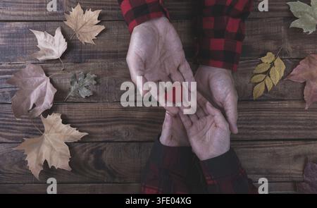 Couple in love holding hands and wooden heart love symbol, autumn leaves on the table Stock Photo
