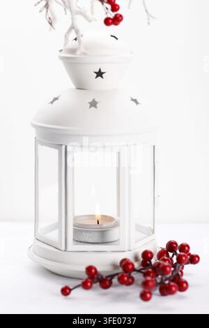 White lantern with candle and branch with berries over white background, vertical Christmas or New year concept Stock Photo