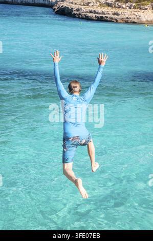 Person cliff jumping and swimming, having fun, in turquoise Mediterranean Sea from rock formations between Platja de S'Amarador and Cala Mondrago beac Stock Photo