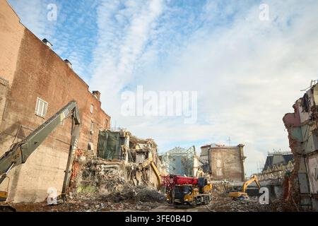 Urban demolition site with heavy machinery under blue sky showing exposed brick building and rubble, with demolition, rubble, excavator, crane detail Stock Photo