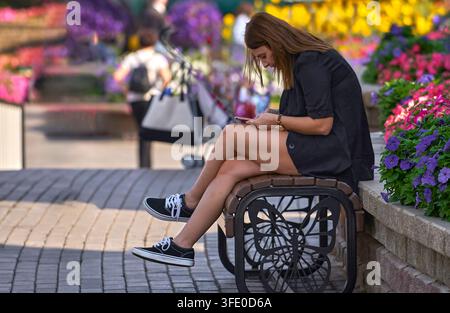 Girl with a phone on the bench in the Miracle Garden of Dubai, UAE Stock Photo