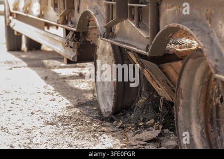 Close-up view of a dirty truck wheel and undercarriage on a dusty road with debris beneath it. Stock Photo