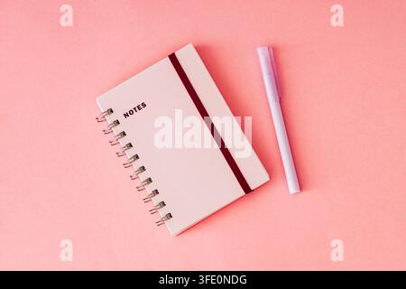 Notebook and pen on pastel pink background. Trendy composition ideal for creative workspaces, office themes, school and education concepts. Stock Photo