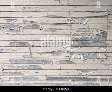 Pale yellow painted lap siding with peeling paint hanging from the boards and a boarded‑up area Stock Photo