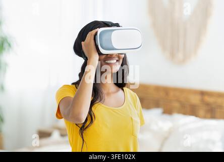 Young black woman in virtual reality headset exploring cyberspace or playing online video game at home Stock Photo