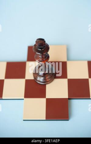 Close-up of a dark wooden chess king standing on a small red and cream chessboard cross against a pale blue background Stock Photo