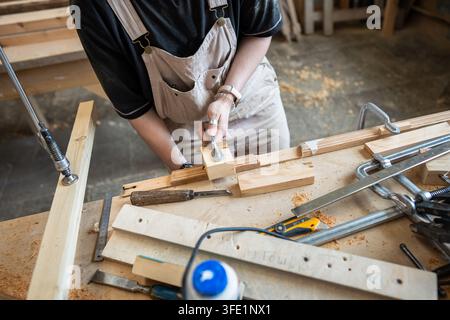 Woman crafter working with wooden blocks and instruments at workbench in restoration workshop Stock Photo