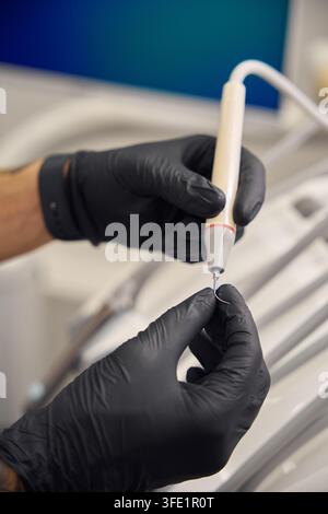 Adult individual, gender-neutral, focused on performing a dental procedure in a sterile dentist's office. Wearing black gloves and holding dental inst Stock Photo