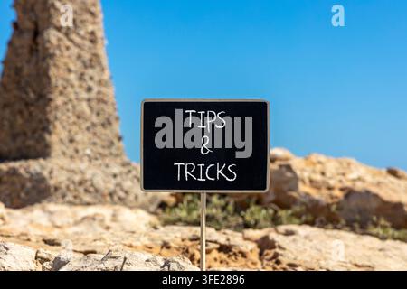 Tips and tricks words symbol. Concept words Tips and tricks on beautiful black blackboard. Beautiful stone and blue sky background. Business tips and Stock Photo