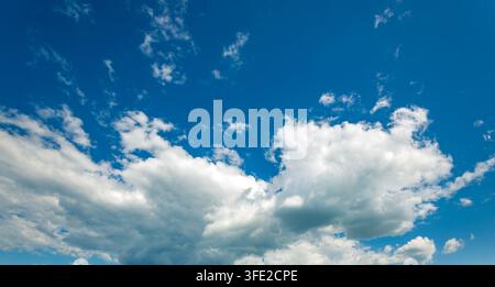 Vast sky painted deep blue with soft clouds. White puffs float gently, light and airy Stock Photo