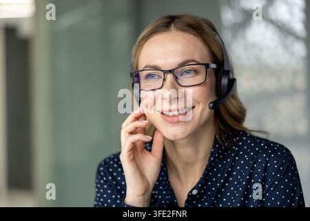 Smiling woman wearing a headset and glasses, providing customer support and assistance, embodying professionalism, communication, and helpdesk concepts in a positive office environment Stock Photo
