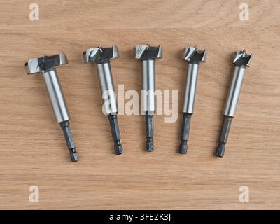 Five Forstner Drill Bits on Wood Surface - Set of five steel Forstner drill bits arranged on a light oak wooden surface, varying sizes for woodworking Stock Photo