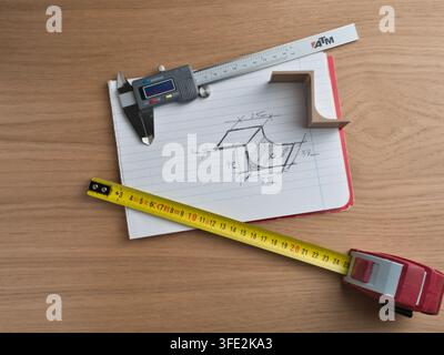 Engineering Tools and Technical Sketch - Digital caliper, tape measure, and ruler surround a hand-drawn technical sketch with dimensions on a wooden d Stock Photo