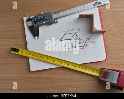 Engineering Tools and Technical Sketch - Digital caliper, tape measure, and ruler surround a hand-drawn technical sketch with dimensions on a wooden d Stock Photo