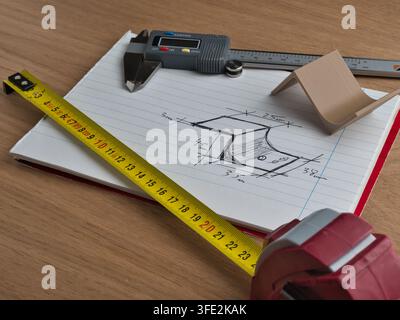 Engineering Tools and Technical Sketch - Digital caliper, tape measure, and ruler surround a hand-drawn technical sketch with dimensions on a wooden d Stock Photo