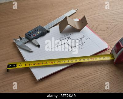 Engineering Tools and Technical Sketch - Digital caliper, tape measure, and ruler surround a hand-drawn technical sketch with dimensions on a wooden d Stock Photo