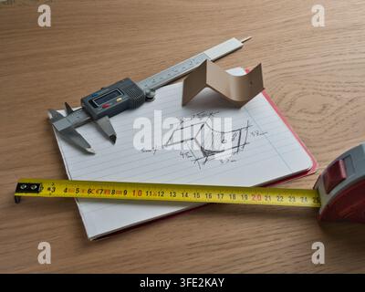 Engineering Tools and Technical Sketch - Digital caliper, tape measure, and ruler surround a hand-drawn technical sketch with dimensions on a wooden d Stock Photo