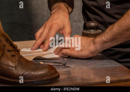 Skilled shoemaker's hands cutting leather on a workbench, with a shoe in progress visible. Precise and methodical gesture typical of Italian artisan s Stock Photo