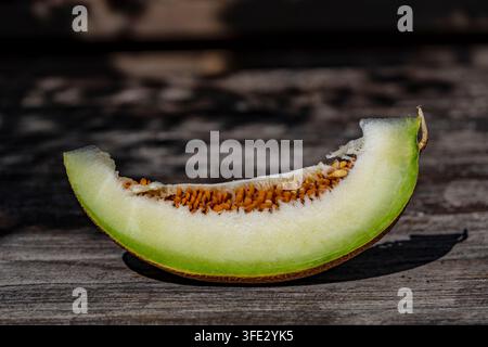 Fresh ripe melon slice with seeds on rustic wooden table outdoors. Close up of single juicy slice of green cantaloupe melon with brown seeds on textur Stock Photo