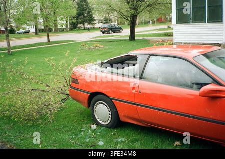 A red coupe with a crushed roof and broken window caused by a fallen tree branch in a residential neighborhood after a storm. Stock Photo